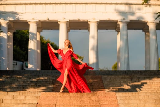 A woman in a long red dress against the backdrop of sunrise, bright golden light of the sun's rays. The concept of femininity, harmony