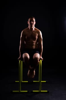 Young muscular man doing parallel bar exercises in a dark white red studio with copy space