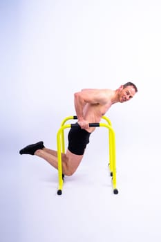 Young muscular man doing parallel bar exercises in a dark white red studio with copy space