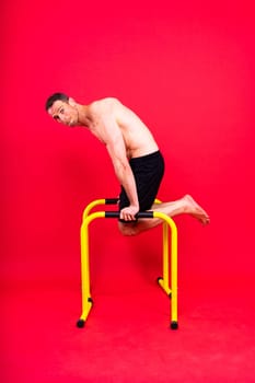 Young muscular man doing parallel bar exercises in a dark white red studio with copy space