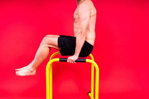 Young muscular man doing parallel bar exercises in a dark white red studio with copy space