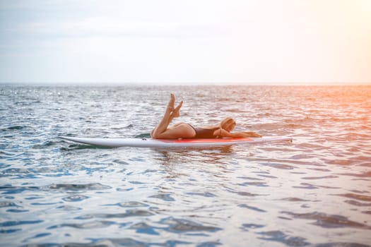 Woman sup sea. Sports girl on a surfboard in the sea on a sunny summer day. In a black bathing suit, he sits on a sapa in the sea. Rest on the sea