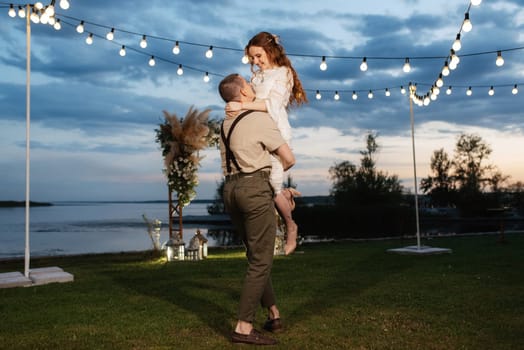 the first wedding dance of the bride and groom in the glade of the country club in the light of sunset and warm garlands