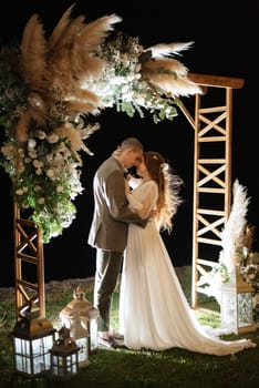 bride and groom against the backdrop of an evening wedding arch with warm live fire