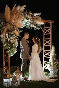 bride and groom against the backdrop of an evening wedding arch with warm live fire