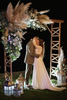 bride and groom against the backdrop of an evening wedding arch with warm live fire