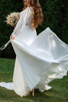 red-haired girl bride with a wedding bouquet on a meadow with green thuja