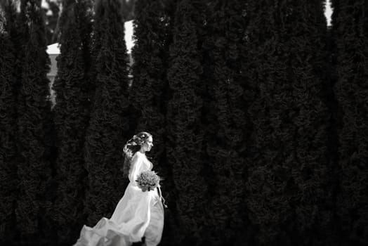 red-haired girl bride with a wedding bouquet on a meadow with green thuja