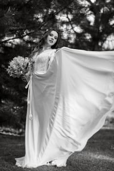 red-haired girl bride with a wedding bouquet on a meadow with green thuja