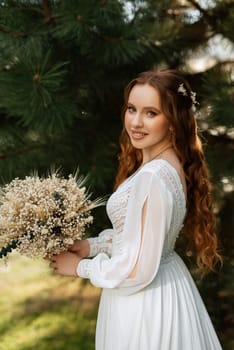 red-haired girl bride with a wedding bouquet on a meadow with green thuja