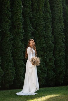 red-haired girl bride with a wedding bouquet on a meadow with green thuja