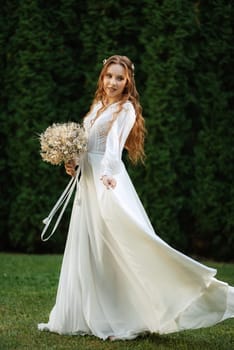 red-haired girl bride with a wedding bouquet on a meadow with green thuja