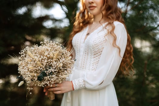 red-haired girl bride with a wedding bouquet on a meadow with green thuja