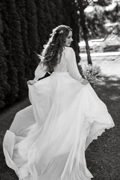 red-haired girl bride with a wedding bouquet on a meadow with green thuja