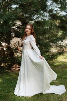 red-haired girl bride with a wedding bouquet on a meadow with green thuja