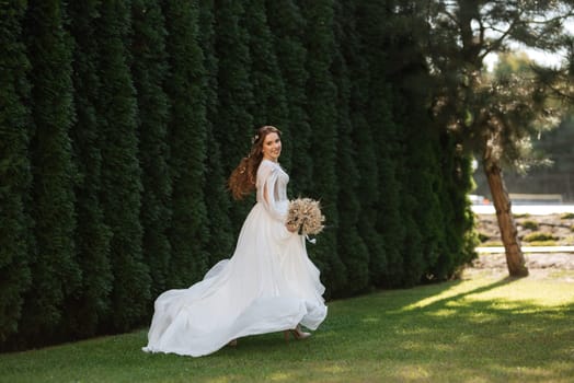 red-haired girl bride with a wedding bouquet on a meadow with green thuja