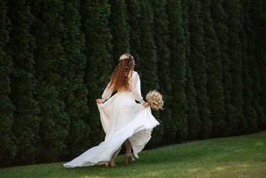 red-haired girl bride with a wedding bouquet on a meadow with green thuja
