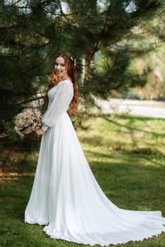 red-haired girl bride with a wedding bouquet on a meadow with green thuja