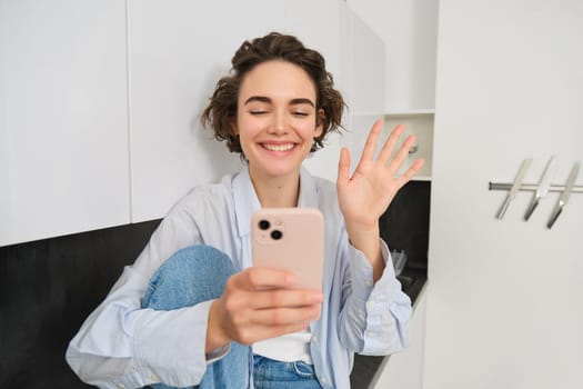 Happy smiling girl, saying hi to a friend on video chat, waves at smartphone app, connects to online conversation on her phone.