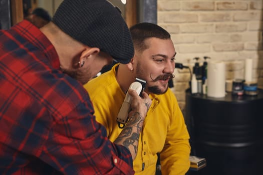 Client with beard and moustache sit on chair, and professional barber make beard shaving in barber shop