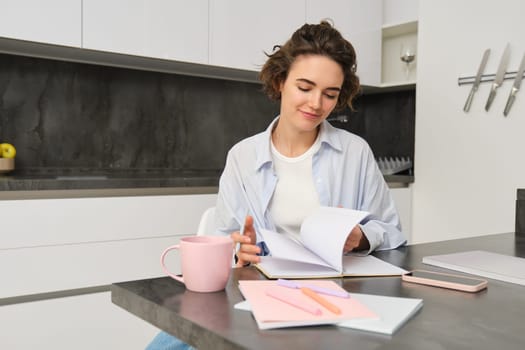 Portrait of young woman at home, working, writing in notebook, taking notes or doing homework.