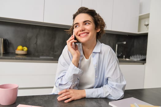 Portrait of cute smiling girl talks on mobile phone, sits at home and calls someone with smartphone.