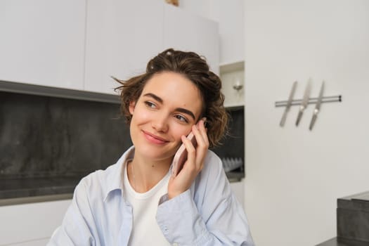 Image of woman working at home, making a phone call, sitting with smartphone, surrounded with paperwork, doing homework and talking to someone.