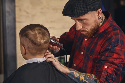 A pretty blonde boy happy to be on the haircut with a professional hairdresser. Blond little boy having a haircut at hair salon. Hairdresser's hands making hairstyle to child at barbershop