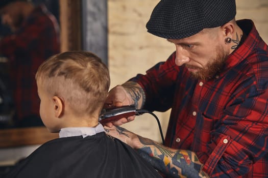 A pretty blonde boy happy to be on the haircut with a professional hairdresser. Blond little boy having a haircut at hair salon. Hairdresser's hands making hairstyle to child at barbershop