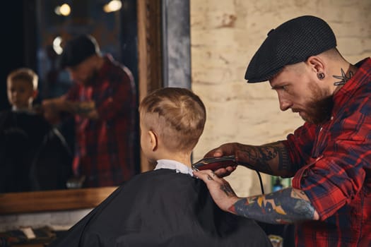 A pretty blonde boy happy to be on the haircut with a professional hairdresser. Blond little boy having a haircut at hair salon. Hairdresser's hands making hairstyle to child at barbershop