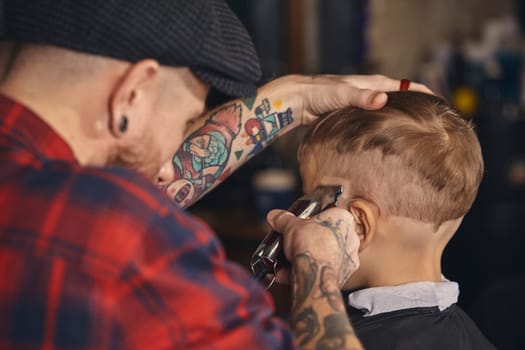 A pretty blonde boy happy to be on the haircut with a professional hairdresser. Blond little boy having a haircut at hair salon. Hairdresser's hands making hairstyle to child at barbershop