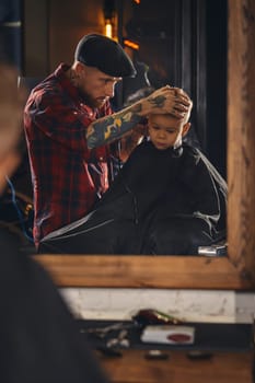 A pretty blonde boy happy to be on the haircut with a professional hairdresser. Blond little boy having a haircut at hair salon. Hairdresser's hands making hairstyle to child at barbershop