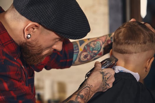 A pretty blonde boy happy to be on the haircut with a professional hairdresser. Blond little boy having a haircut at hair salon. Hairdresser's hands making hairstyle to child at barbershop