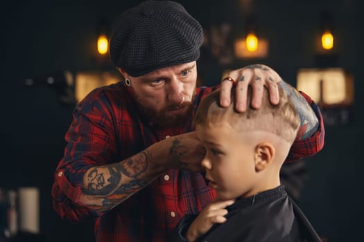 A pretty blonde boy happy to be on the haircut with a professional hairdresser. Blond little boy having a haircut at hair salon. Hairdresser's hands making hairstyle to child at barbershop