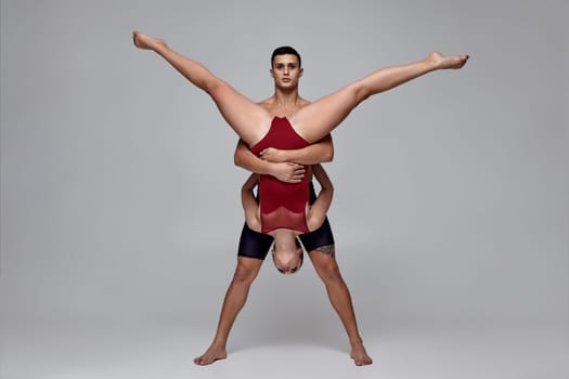 The couple of a young modern ballet dancers are posing over a gray studio background. Man in black shorts and woman in a red swimwear are dancing together. Ballet and contemporary choreography concept. Art photo.