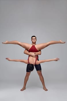 Two young sporty ballet dancers are posing over a gray studio background. Male in black shorts and female in a wonderful red swimwear are dancing together. Ballet and contemporary choreography concept. Art photo.