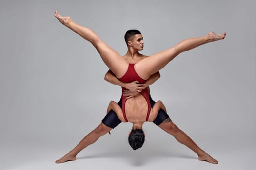 The couple of a strong ballet dancers are posing over a gray studio background. Male in black shorts and girl in a bright red swimwear are dancing together. Ballet and contemporary choreography concept. Art photo.