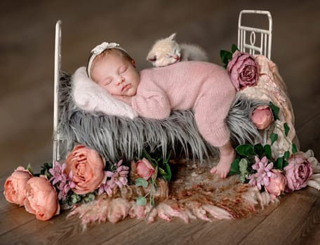 Newborn baby girl with a kitty sleeping in a tiny bed with peony flower decoration. Cute infant child kid napping floral spring portrait
