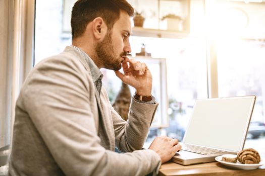 Young businessman on a break in a cafe. He is working at laptop and thinking. 