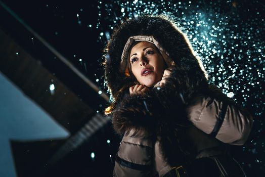 Beautiful young woman in winter jacket with fur hood worries and is looking away waiting for somebody.