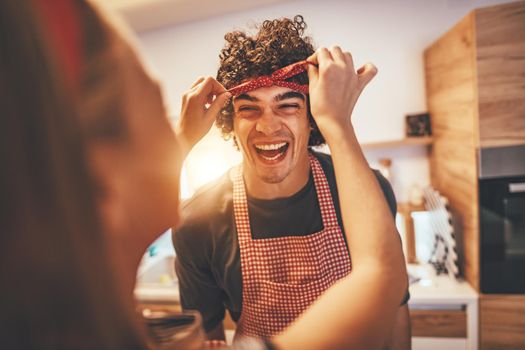 Happy father and his daughter enjoy and having fun in making and having healthy meal together at their home kitchen. The girl binds the ribbon around her father's head