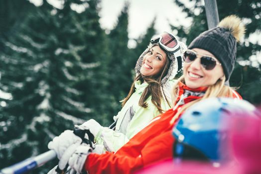 Beautiful young woman friends enjoying in winter vacations. They driving on ski lift and looking at camera with smile.