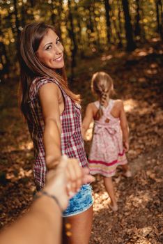 Beautiful young smiling mother and her daughter walking through autumn forest. 
