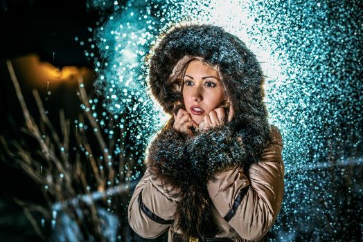 Beautiful young scared woman in winter jacket with fur hood worries and is looking away waiting for somebody.