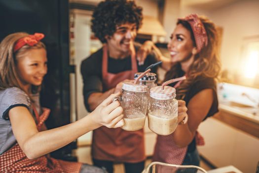 Young smiling family is toasting with fruit smoothie in the kitchen.