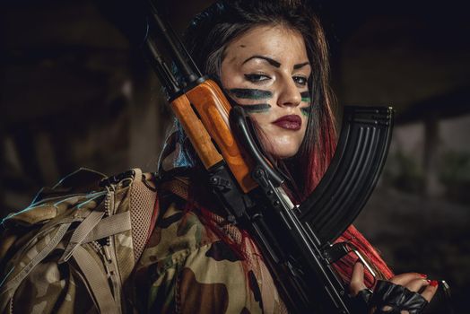 Attractive dark-haired girl in camouflage shirt hold machine gun leaning on the shoulder and with a dangerous expression on her face looking at the camera.