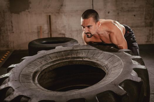 Young muscular man flipping a tire on cross fit training at the gym.