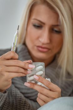 Close-up of female hands with long nails holding a thermometer and medicine, face blond girl is out of focus.