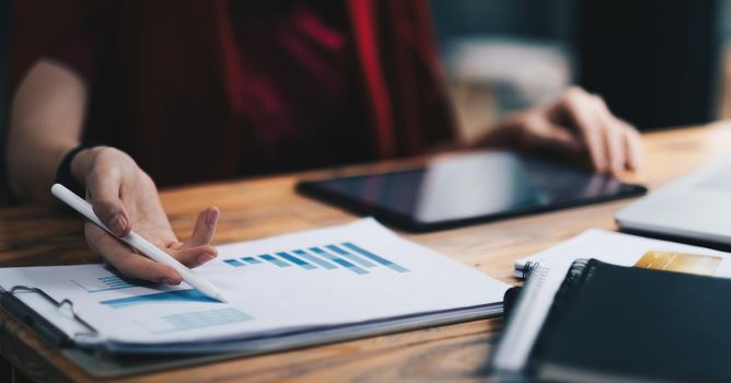 Close up business woman holding pen and pointing paper chart summary analyzing annual business report with using laptop at room office desk.