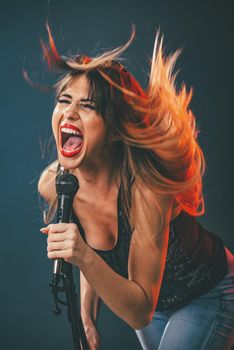 A young woman singer with tousled long hair holding a microphone and sing with a wide open mouth.